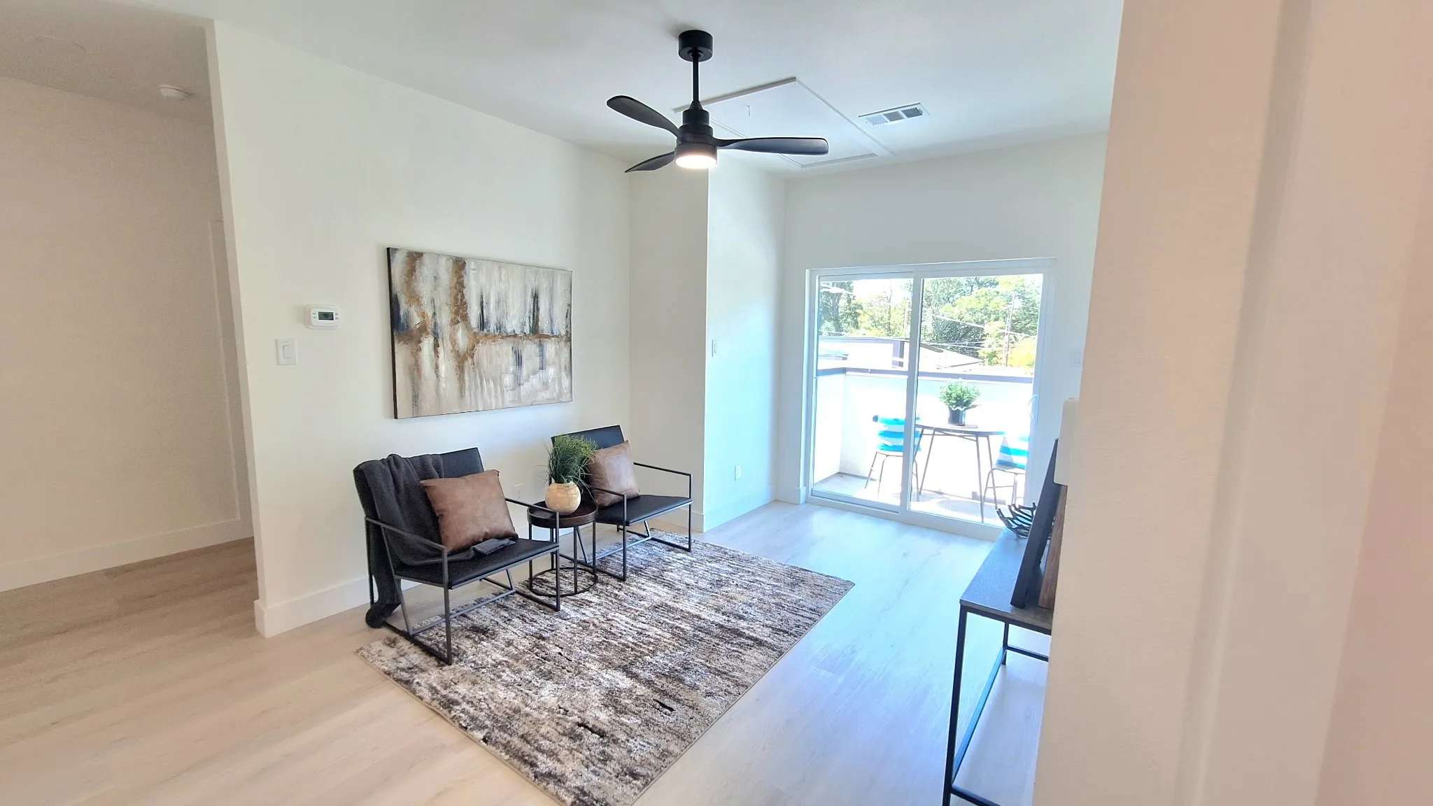 Light wood-finish flooring, white walls, black ceiling fan, and sliding glass door leading to a balcony