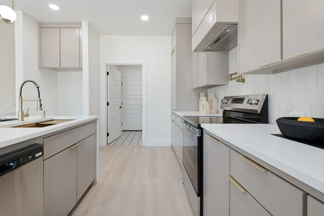 Contemporary kitchen featuring light wood-finish flooring, white countertops, gray cabinetry with gold-tone hardware, and a white geometric tile backsplash