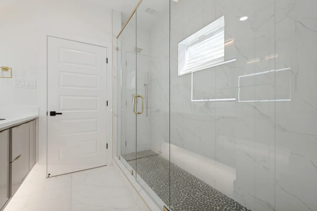 Glass-enclosed shower with pebble-tile floor and gold-finish hardware