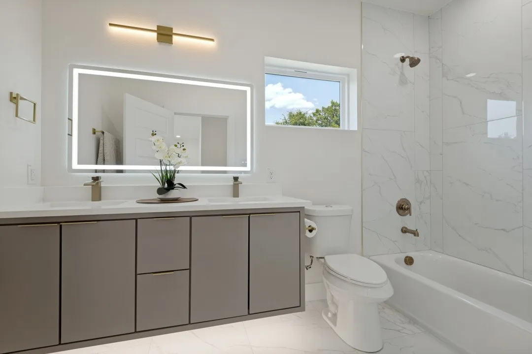 Dual vanity with integrated sinks, quartz countertop, illuminated mirror, and modern cabinetry