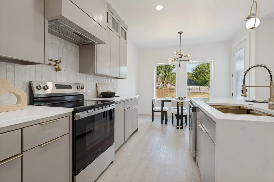 Modern kitchen featuring light gray cabinetry, stainless steel appliances, a white tile backsplash, and light wood-finish flooring