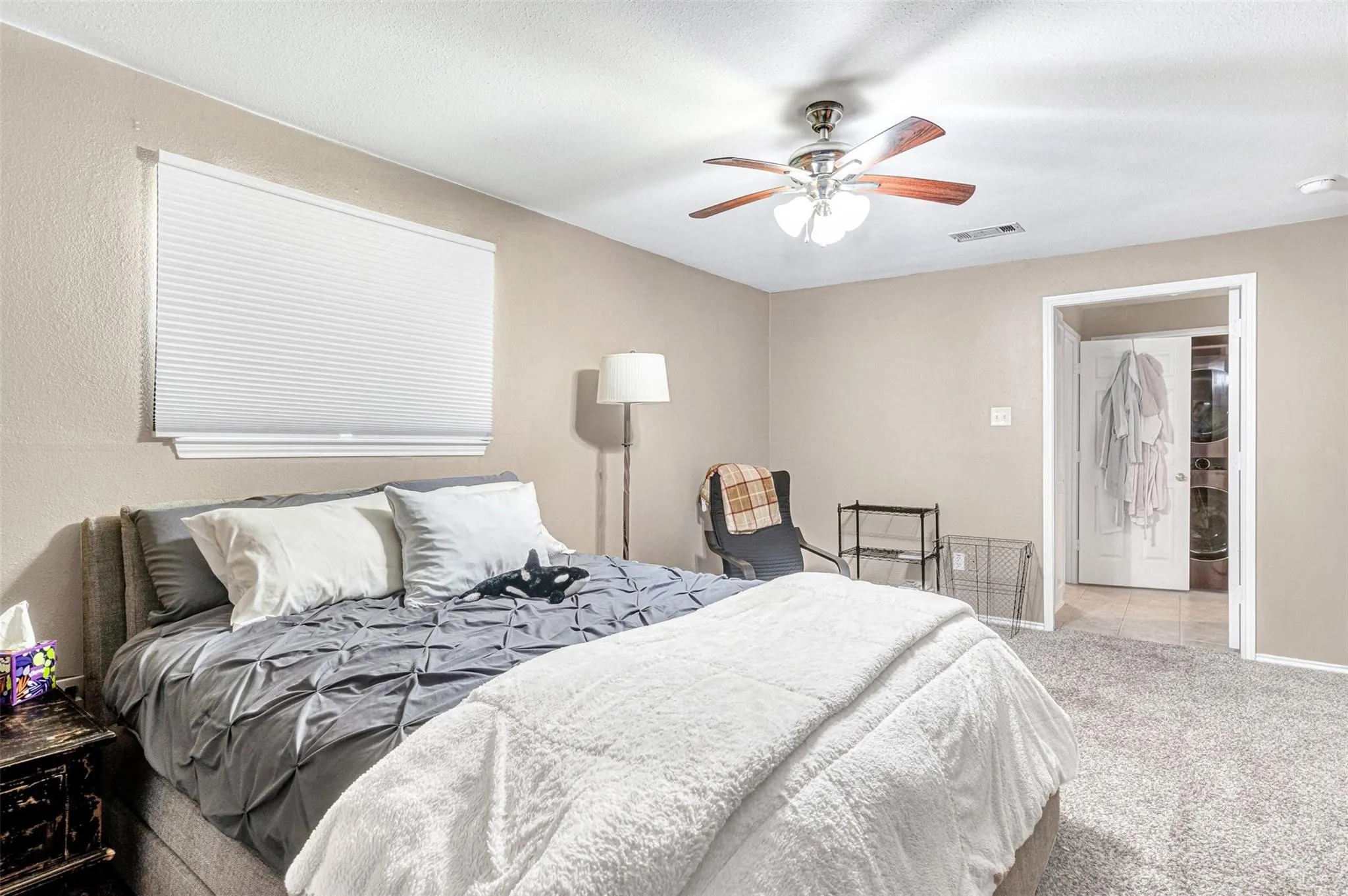 Spacious primary bedroom with neutral wall finishes, carpet flooring, and abundant natural light from a large window with horizontal blinds