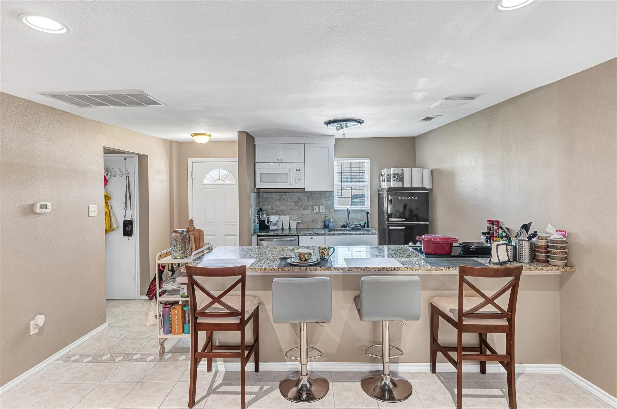 Kitchen featuring white cabinetry, a light-toned backsplash, and a breakfast bar with a stone-finish countertop