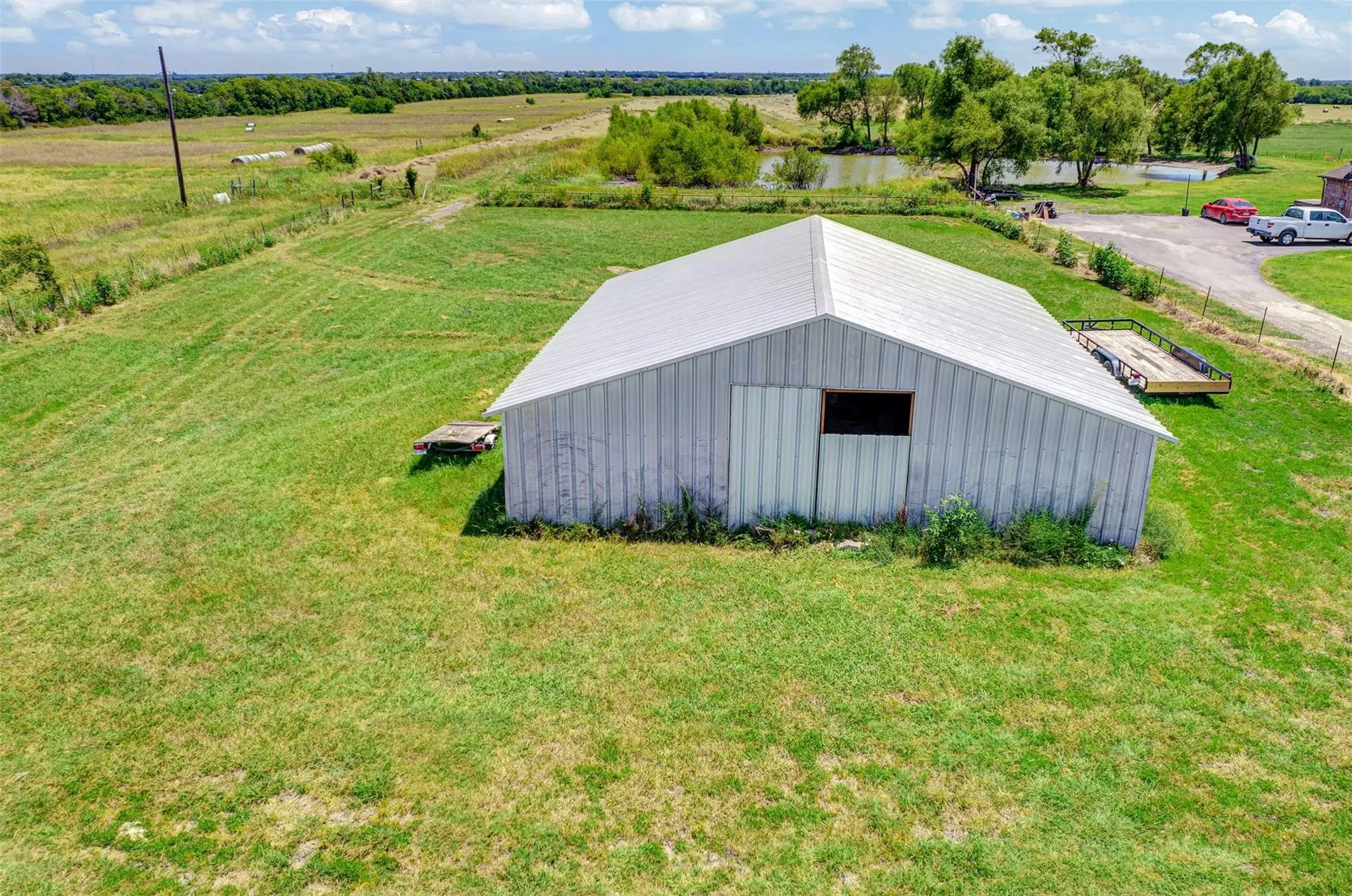 Metal barn structure with a gable roof, surrounded by green landscaping