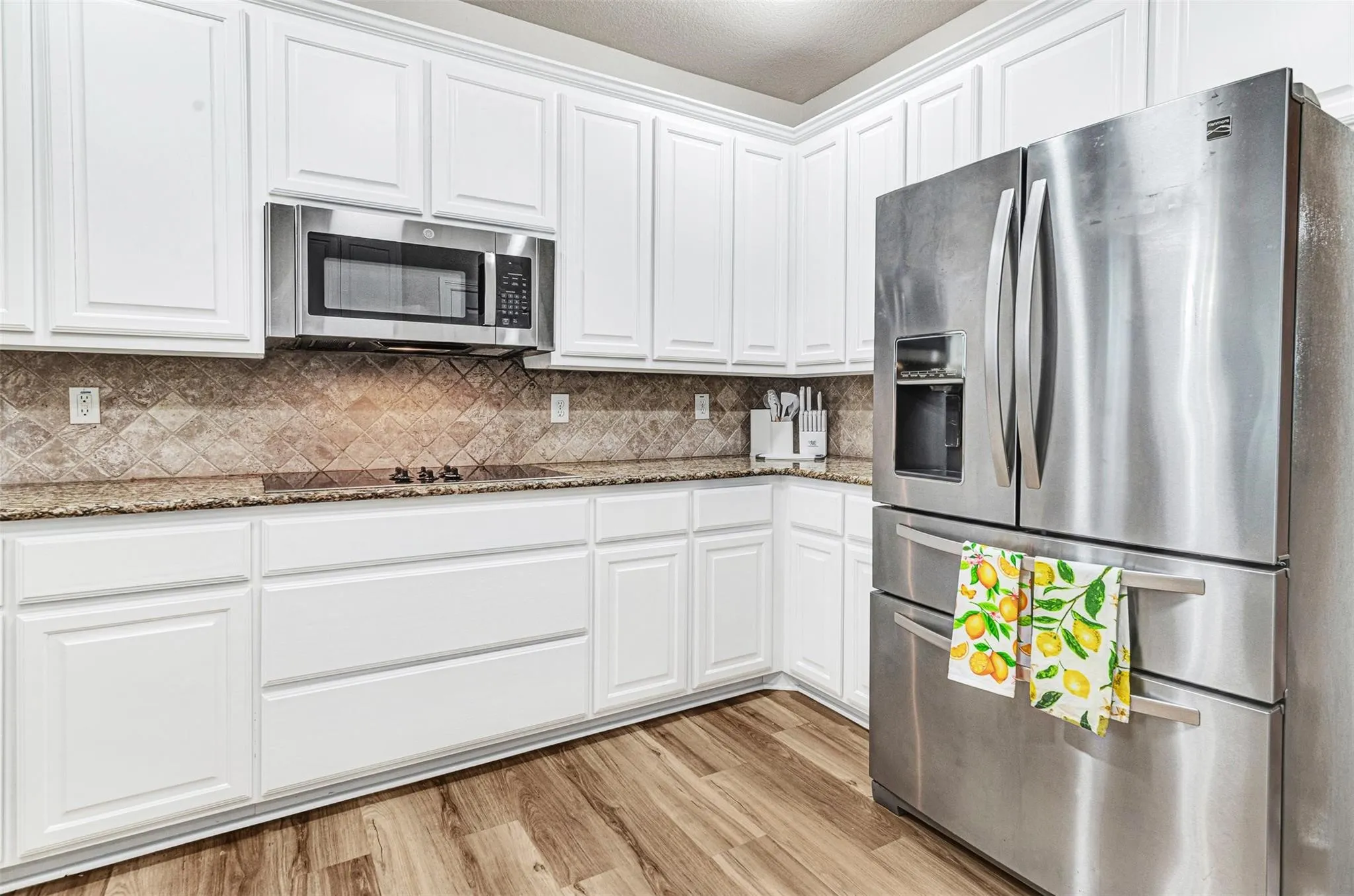 Modern kitchen featuring white raised-panel cabinetry, stainless steel French-door refrigerator with bottom freezer drawers, and integrated stainless steel appliances including a microwave and wall oven