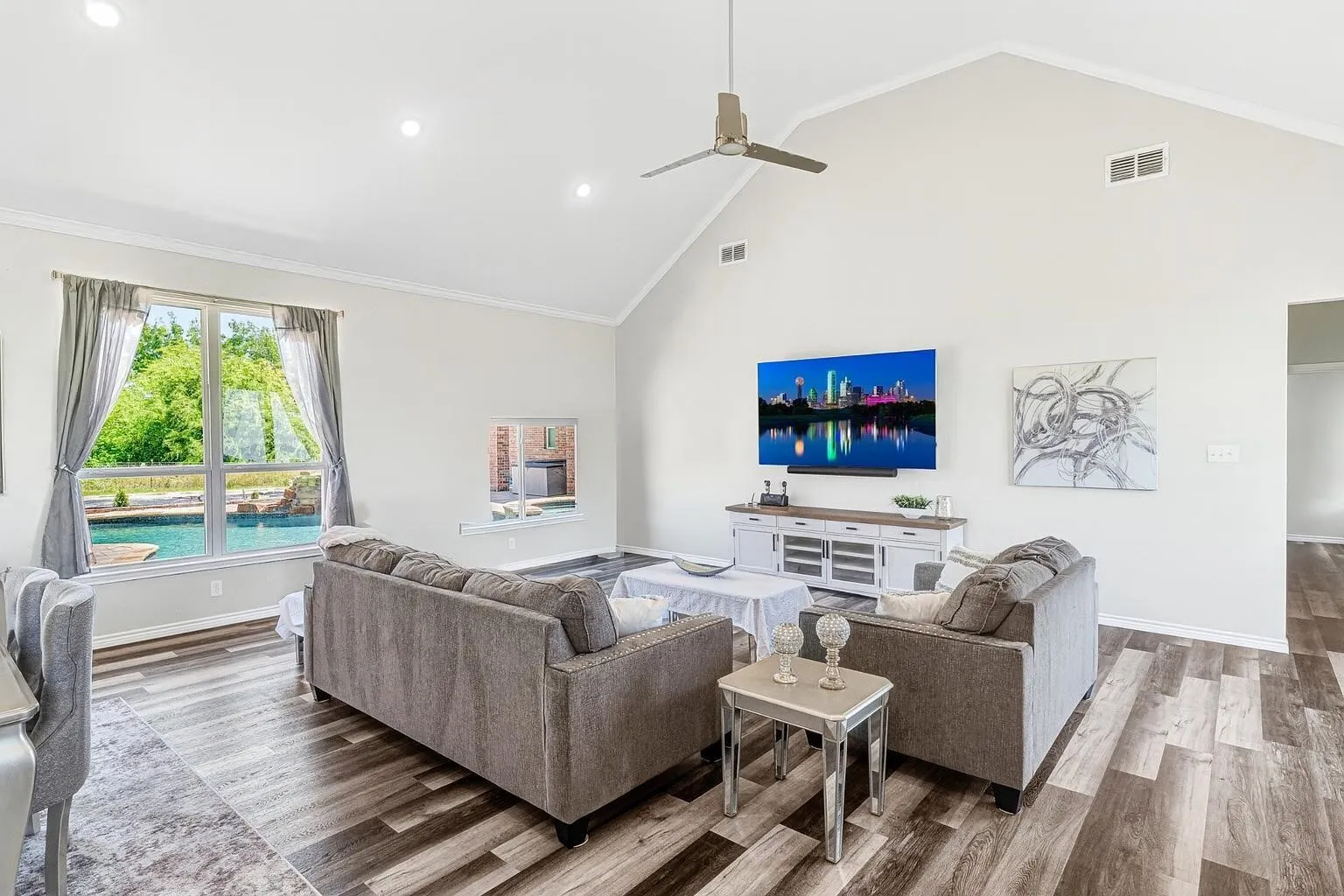 Bright, open-concept living area featuring wood-finish flooring, vaulted ceilings with ceiling fan, and expansive windows with natural light