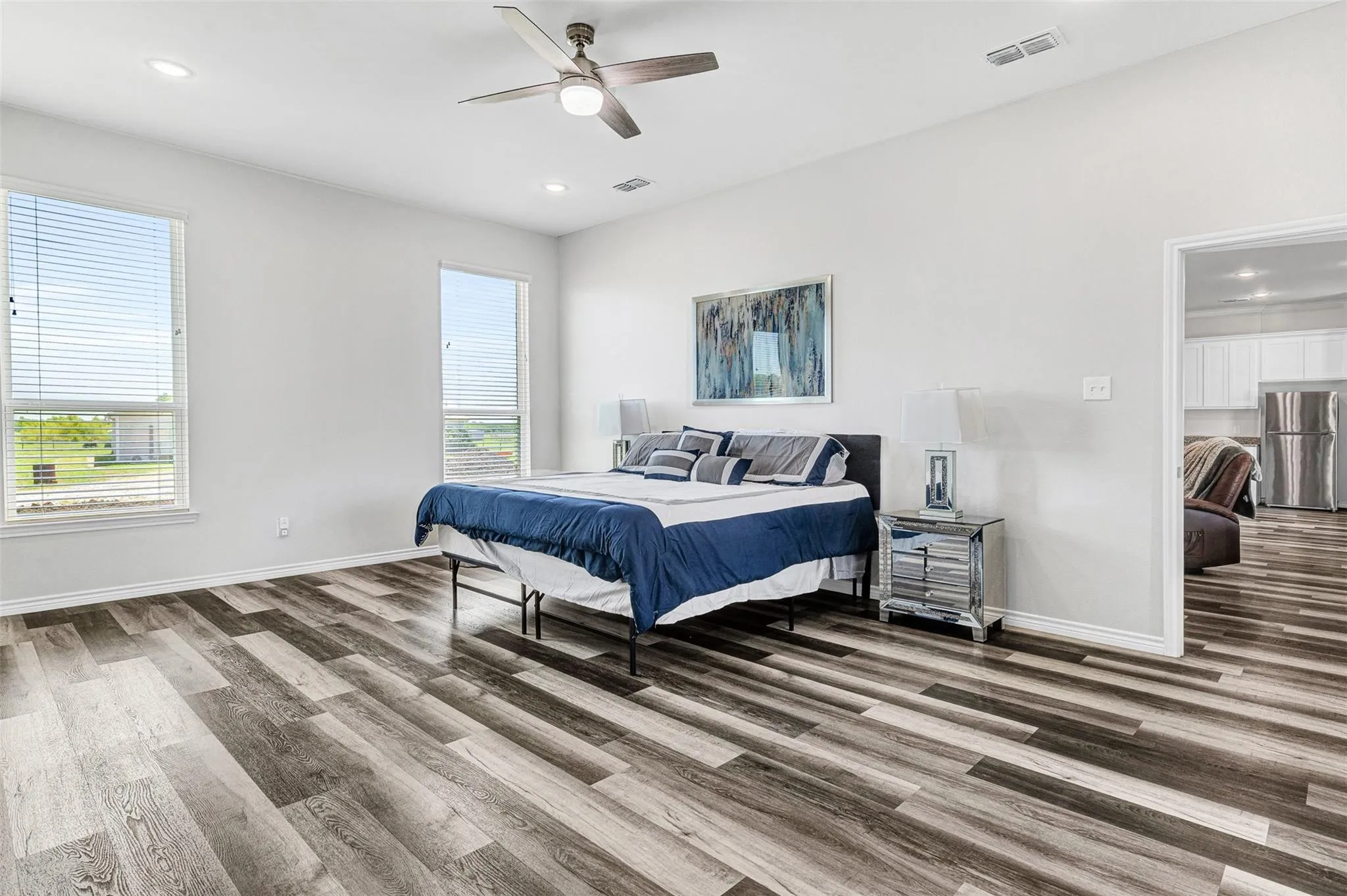 Spacious primary bedroom featuring wood-finish plank flooring, abundant natural light from dual windows, ceiling fan with integrated lighting, and a convenient ensuite bathroom accessible through the adjacent doorway