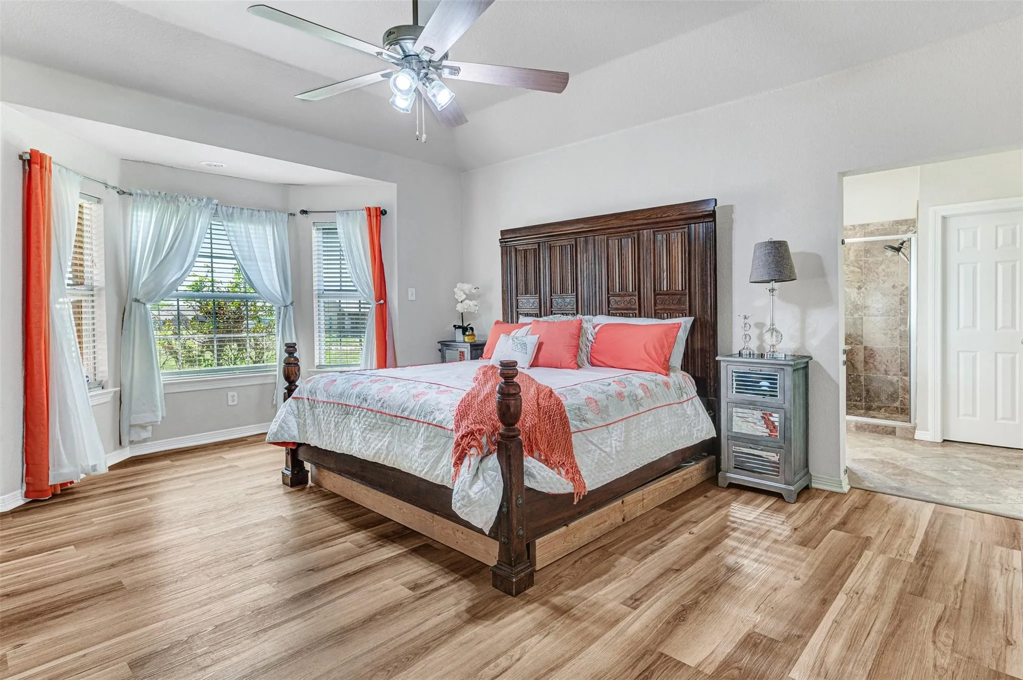 Spacious primary bedroom featuring a wood-finish plank floor, ceiling fan with integrated lighting, and large windows with shutters and layered window treatments