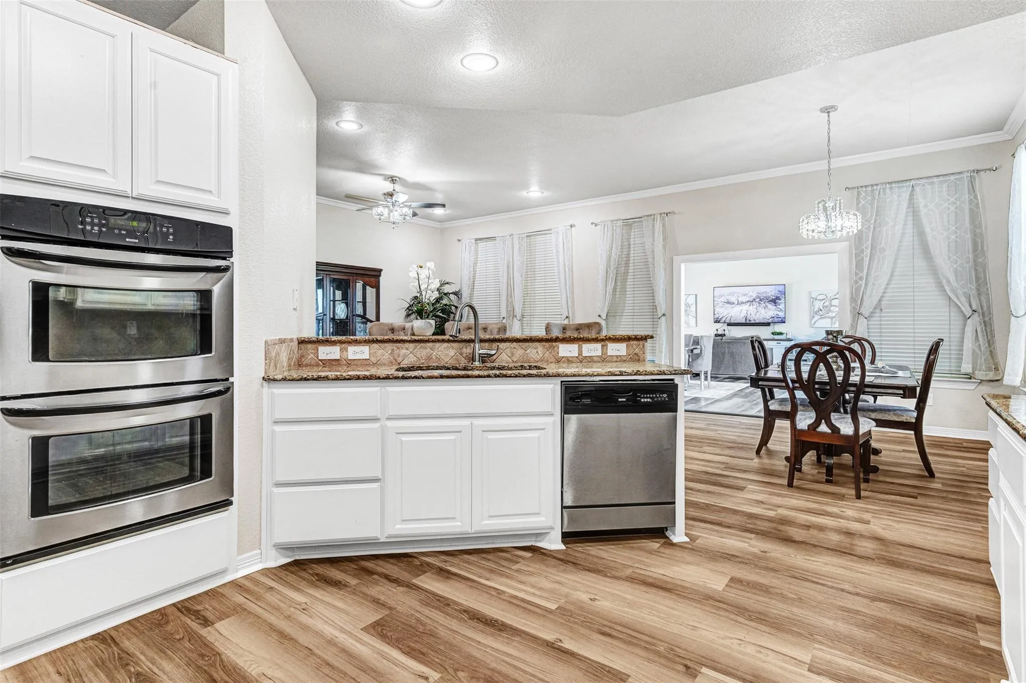Kitchen featuring stainless steel double ovens, white cabinetry, wood-finish flooring, and a dishwasher