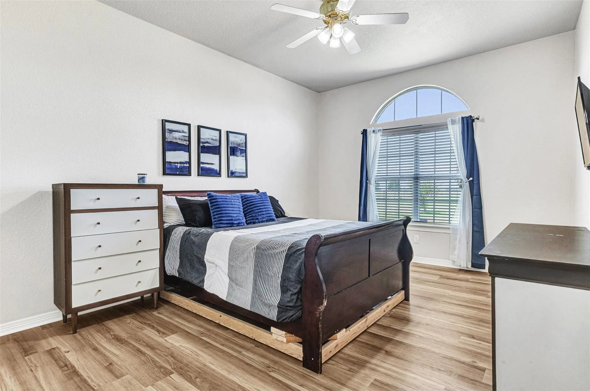 Bright interior with vaulted ceiling, wood-finish flooring, arched window, and ceiling fan
