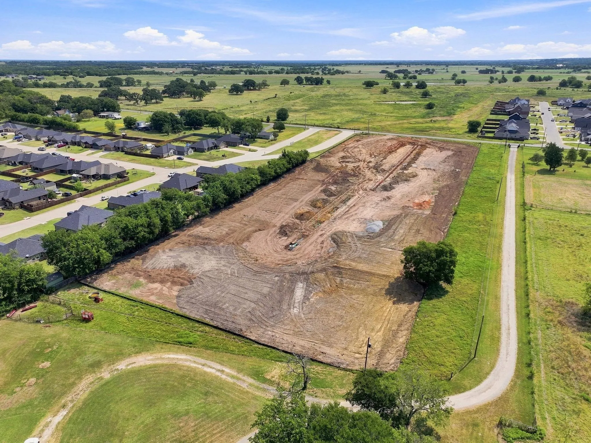Expansive cleared land parcel with surrounding green spaces, bordered by established residential properties