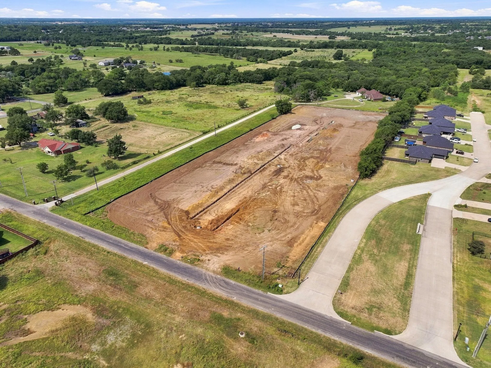 Cleared lot with visible trenching and a paved street frontage, situated within a developed residential area