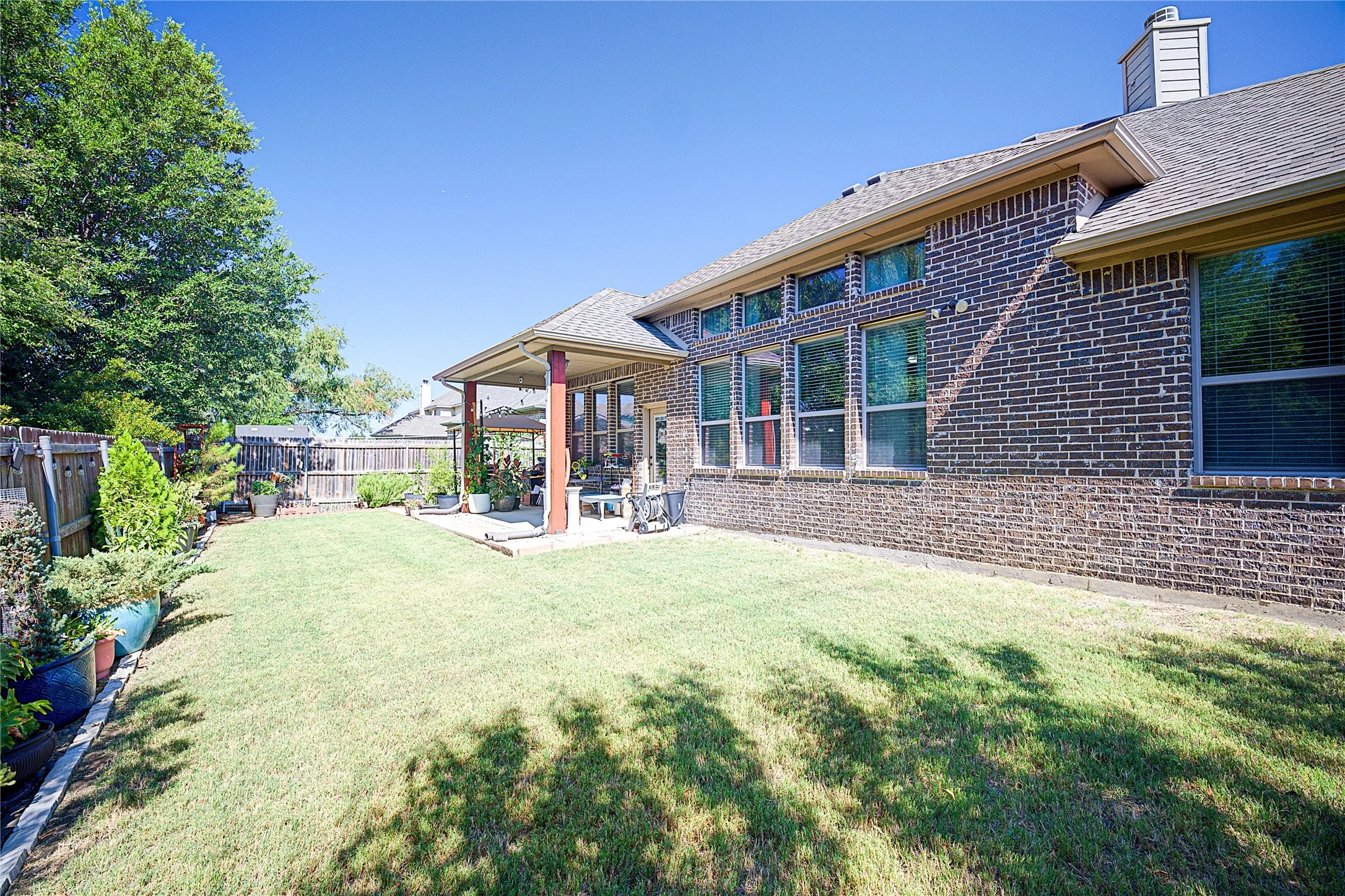 Expansive backyard with a covered patio, brick exterior, multiple windows, and a privacy fence