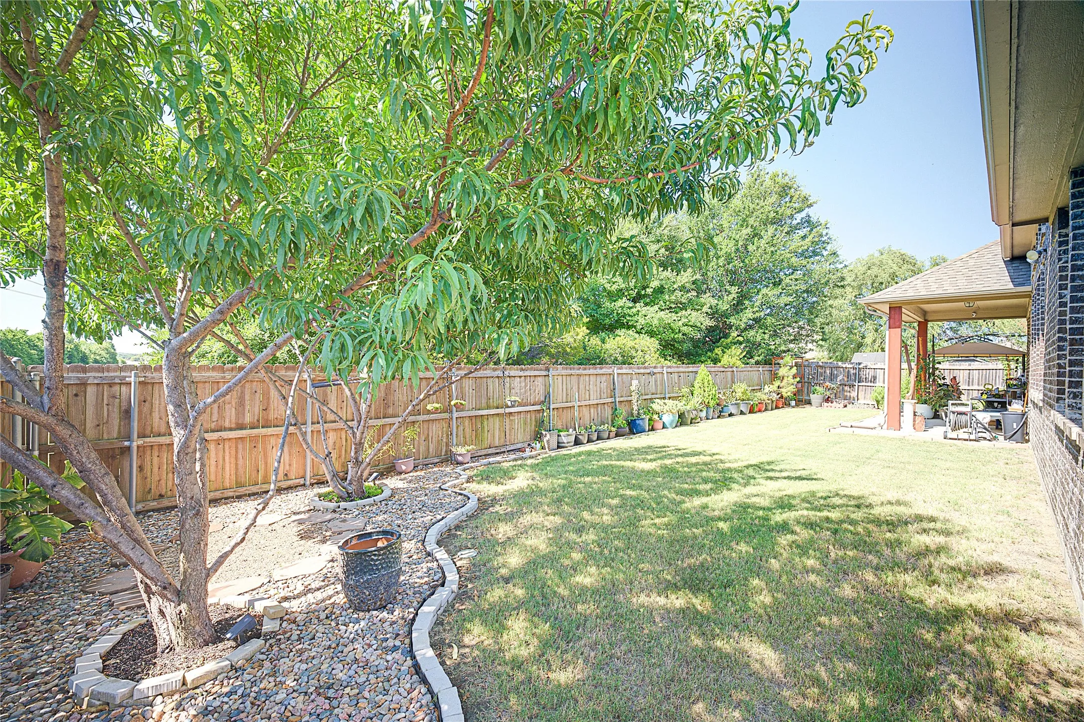 Expansive backyard featuring a manicured lawn, established trees, a wood privacy fence, and a covered patio with brick columns