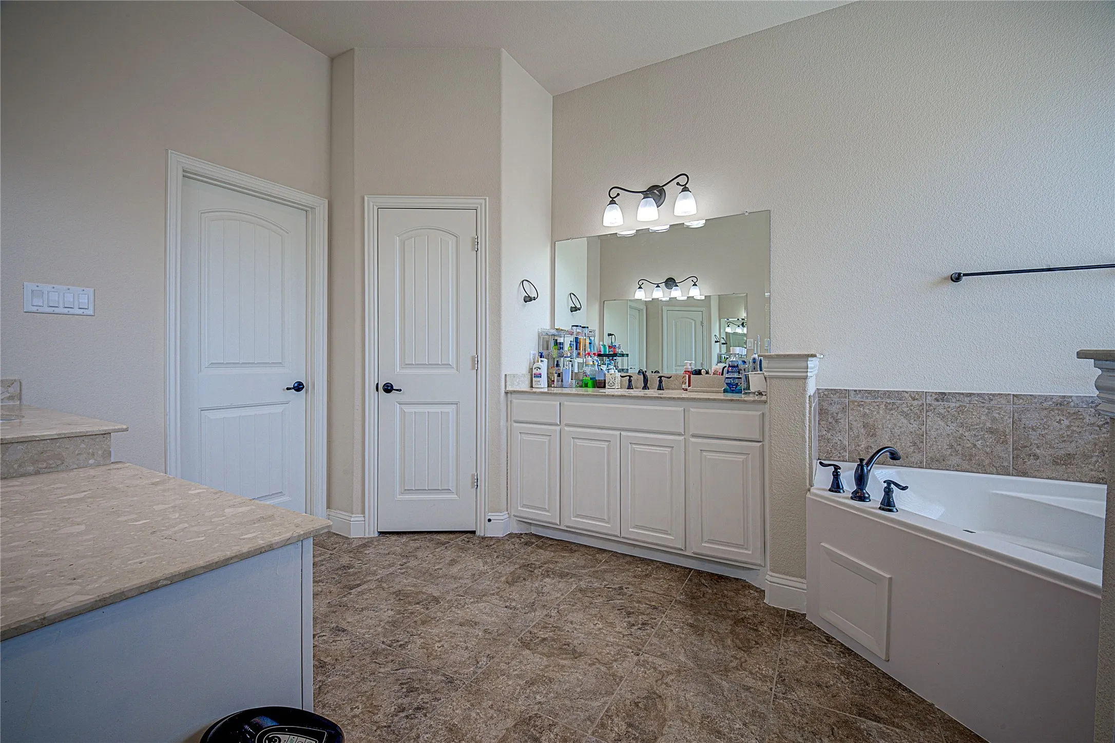 Double vanity with white cabinetry, built-in bathtub with tile surround, and wood-finish flooring