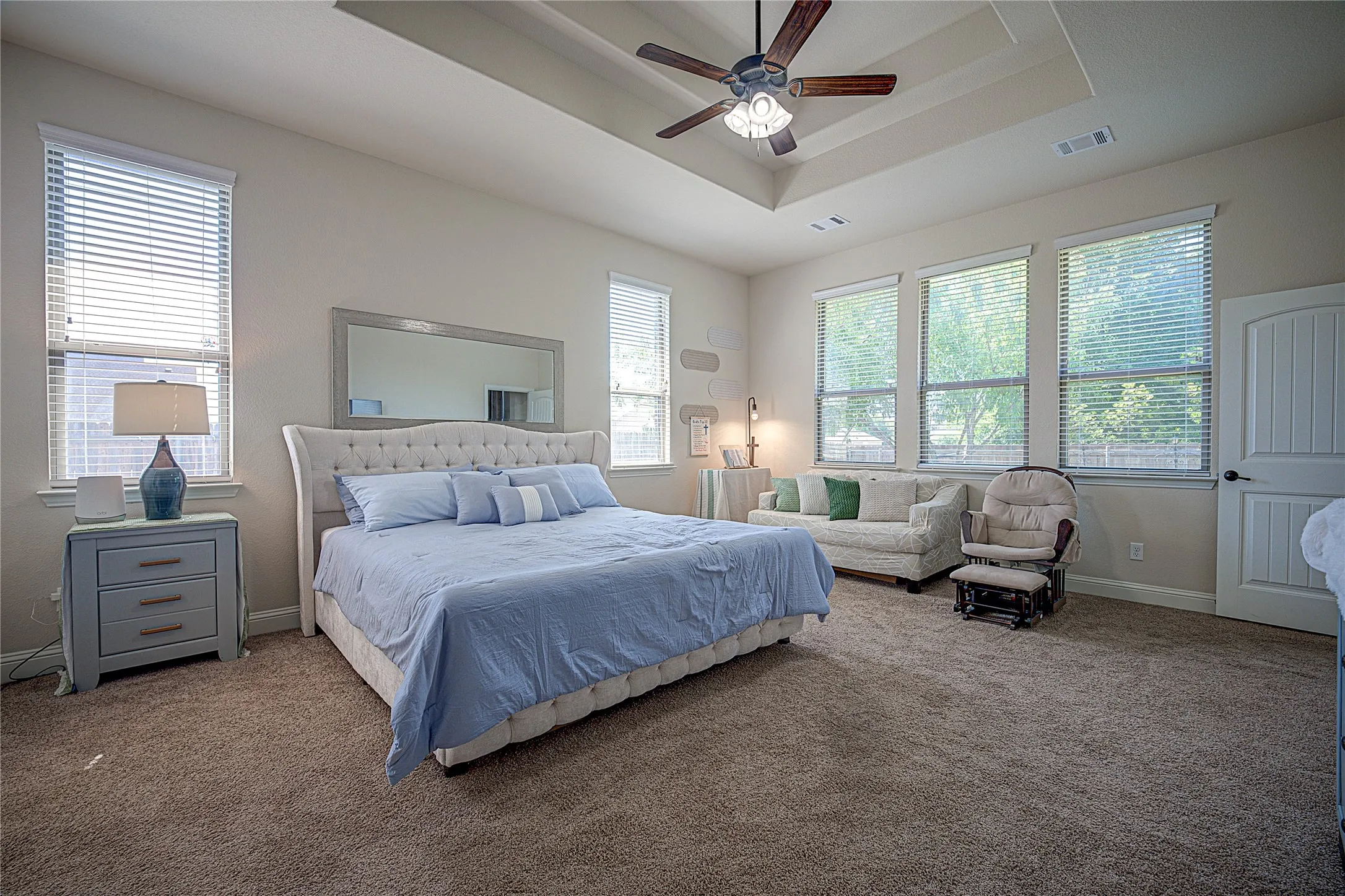 Tray ceiling with a ceiling fan, multiple windows with blinds, and carpeted flooring