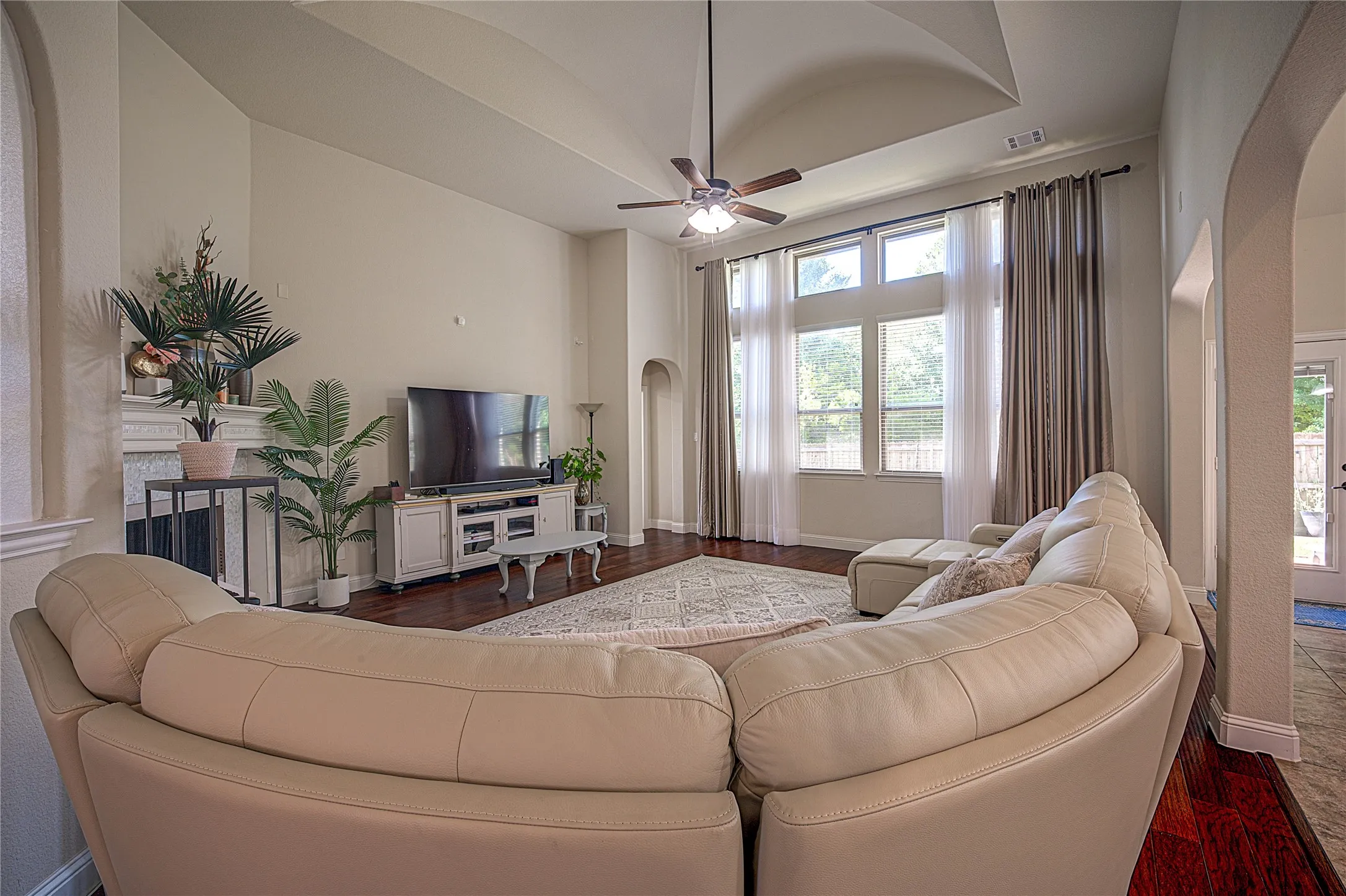 Tray ceiling with a ceiling fan, wood-finish flooring, and a fireplace with a mantel