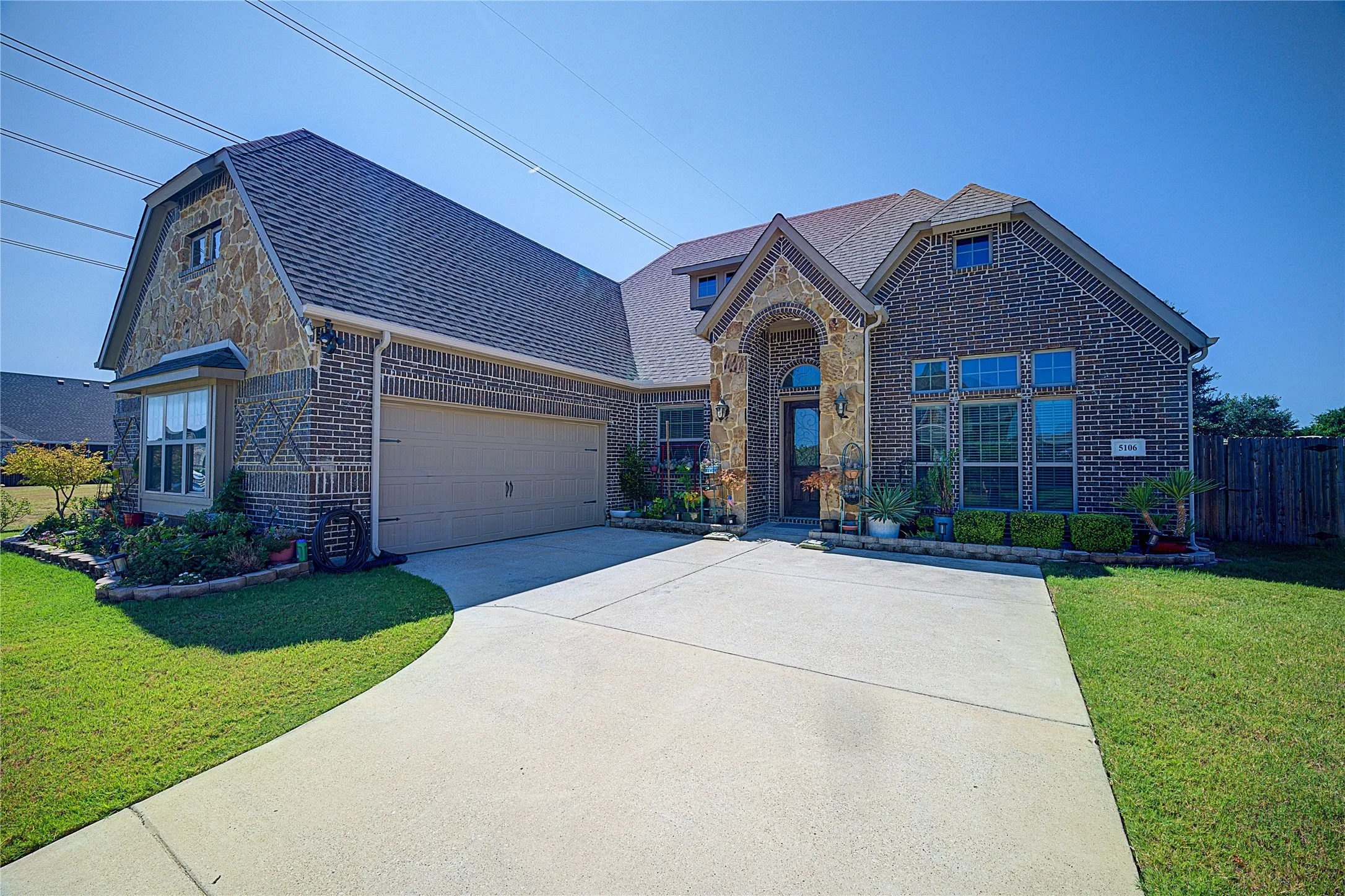 Brick and stone exterior featuring an arched entryway, gabled roofline, two-car garage, and concrete driveway