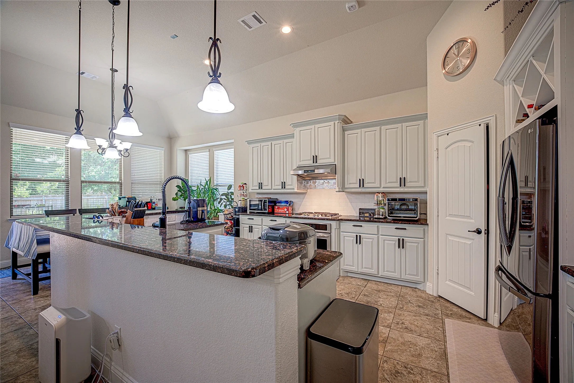 Kitchen featuring white cabinetry, dark stone countertops, pendant lighting, stainless steel appliances, and tile flooring
