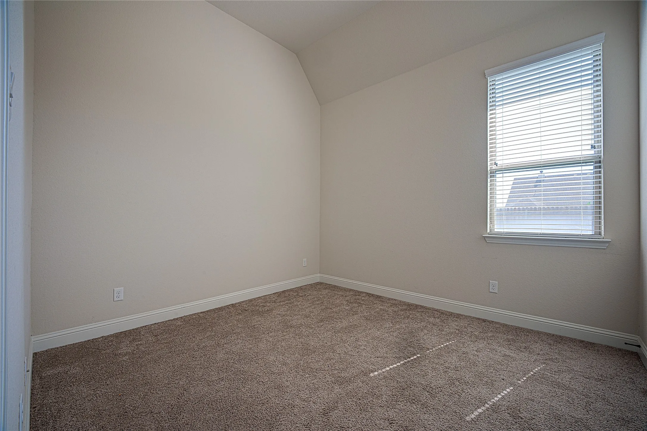 Neutral wall color, angled ceiling, window with blinds, and carpeting