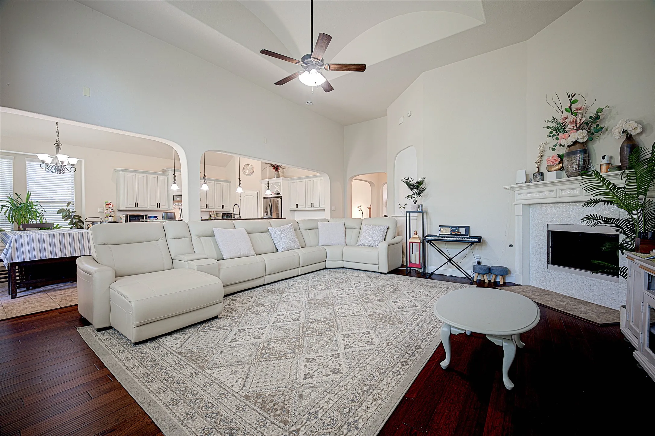 Vaulted ceiling with a ceiling fan, fireplace with a decorative mantel and mosaic tile surround, rich wood-finish flooring, and arched architectural details