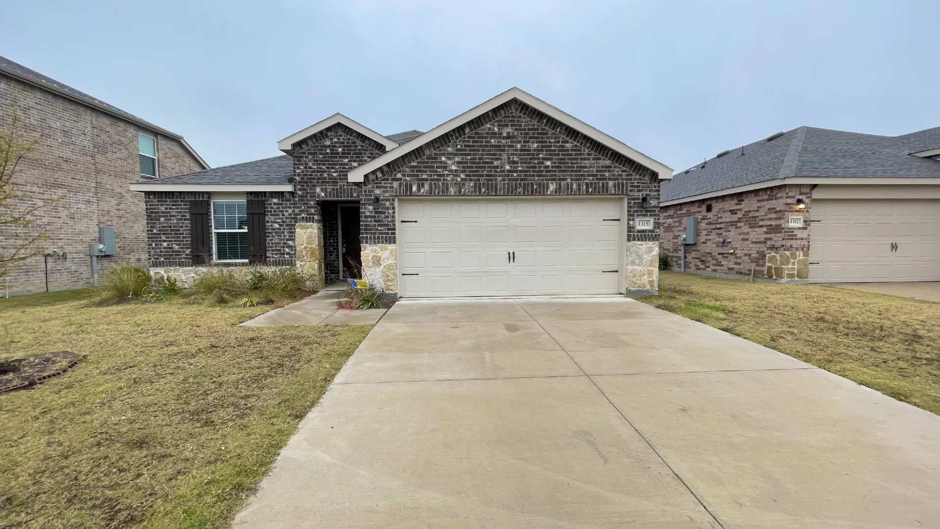 Brick and stone facade featuring decorative shutters, an attached two-car garage, and a concrete driveway
