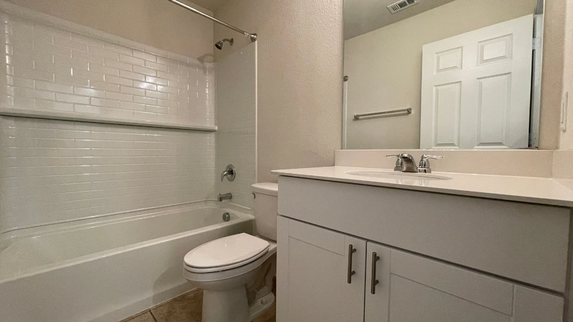 Bright, updated bathroom featuring crisp white subway tile surround with horizontal stripe detailing, a vanity with dual cabinet storage and brushed nickel hardware, a wide countertop with integrated sink, and a toilet with elongated bowl