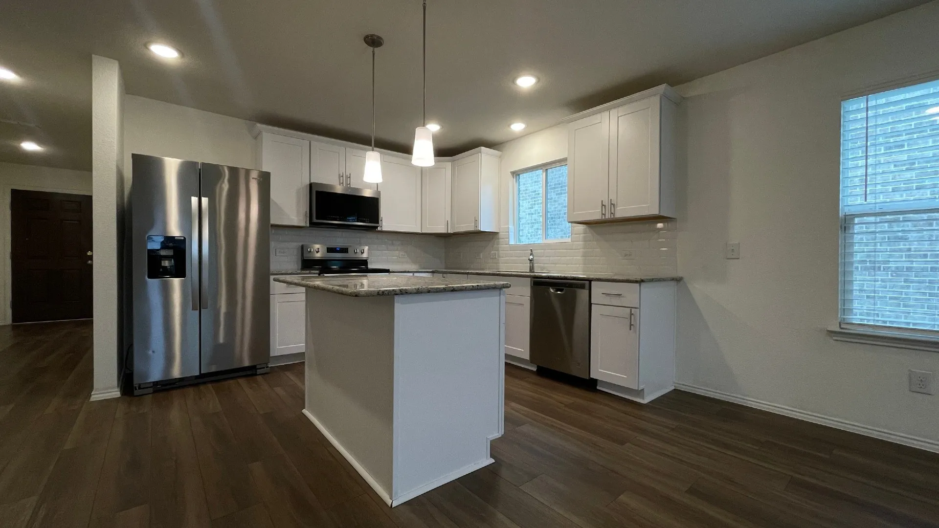 Modern kitchen featuring stainless steel appliances, white cabinetry with ample storage, waterfall-edge island with seating, and wood-finish flooring throughout