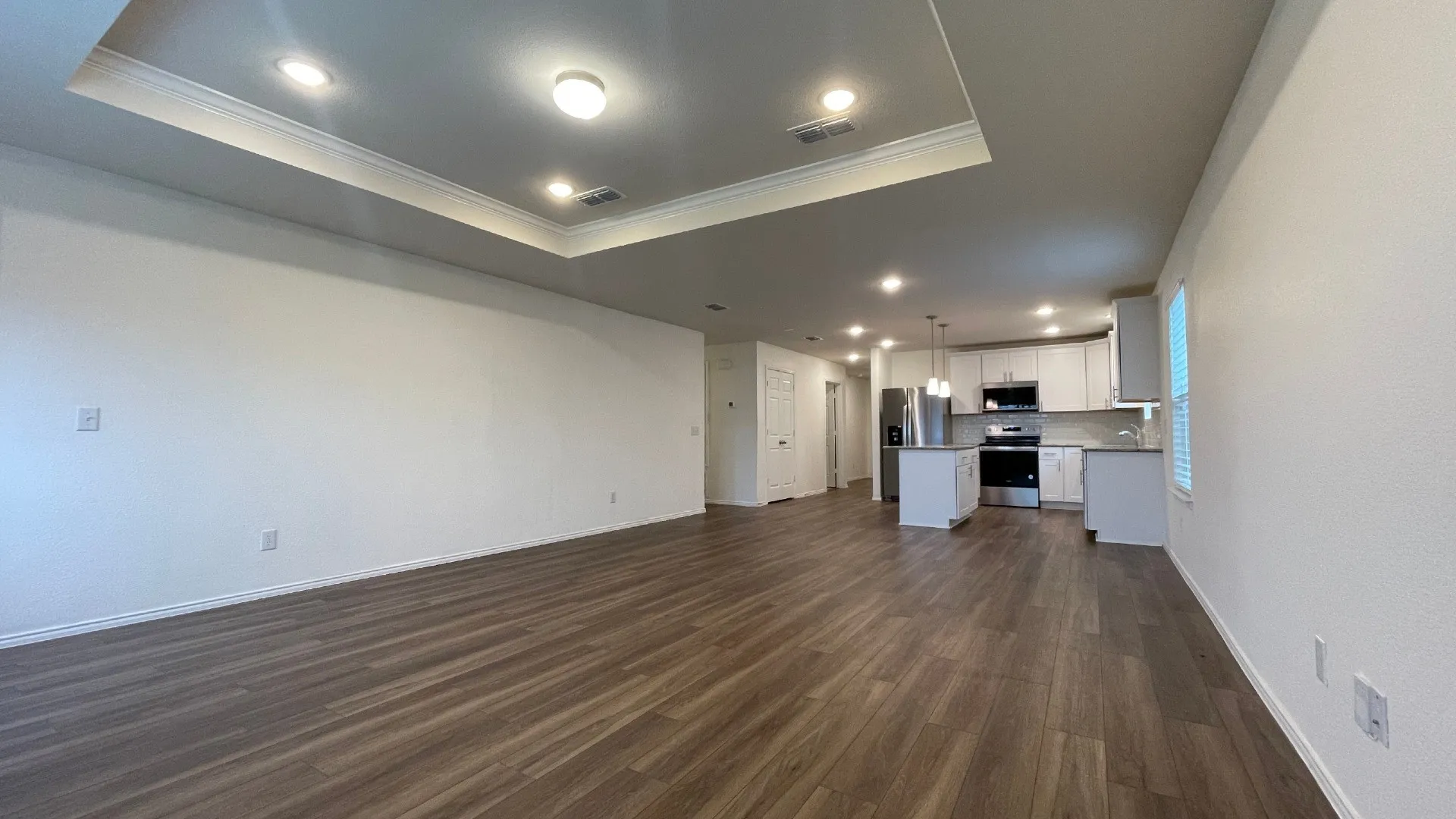 Open-concept living and kitchen area featuring recessed ceiling lighting, a coffered ceiling detail, wood-finish flooring throughout, and built-in kitchen cabinetry with integrated appliances