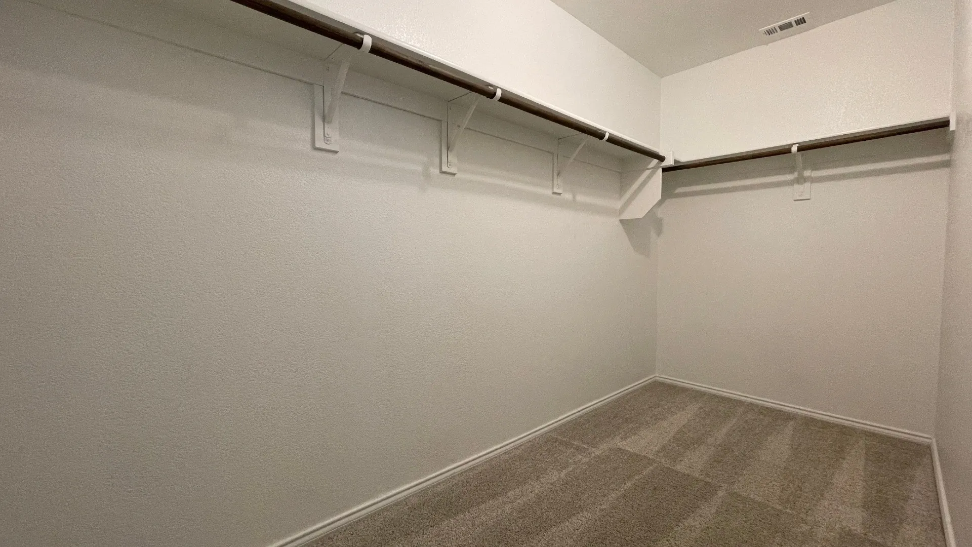 Spacious walk-in closet featuring light-colored walls, carpeted flooring, and built-in shelving with hanging rods