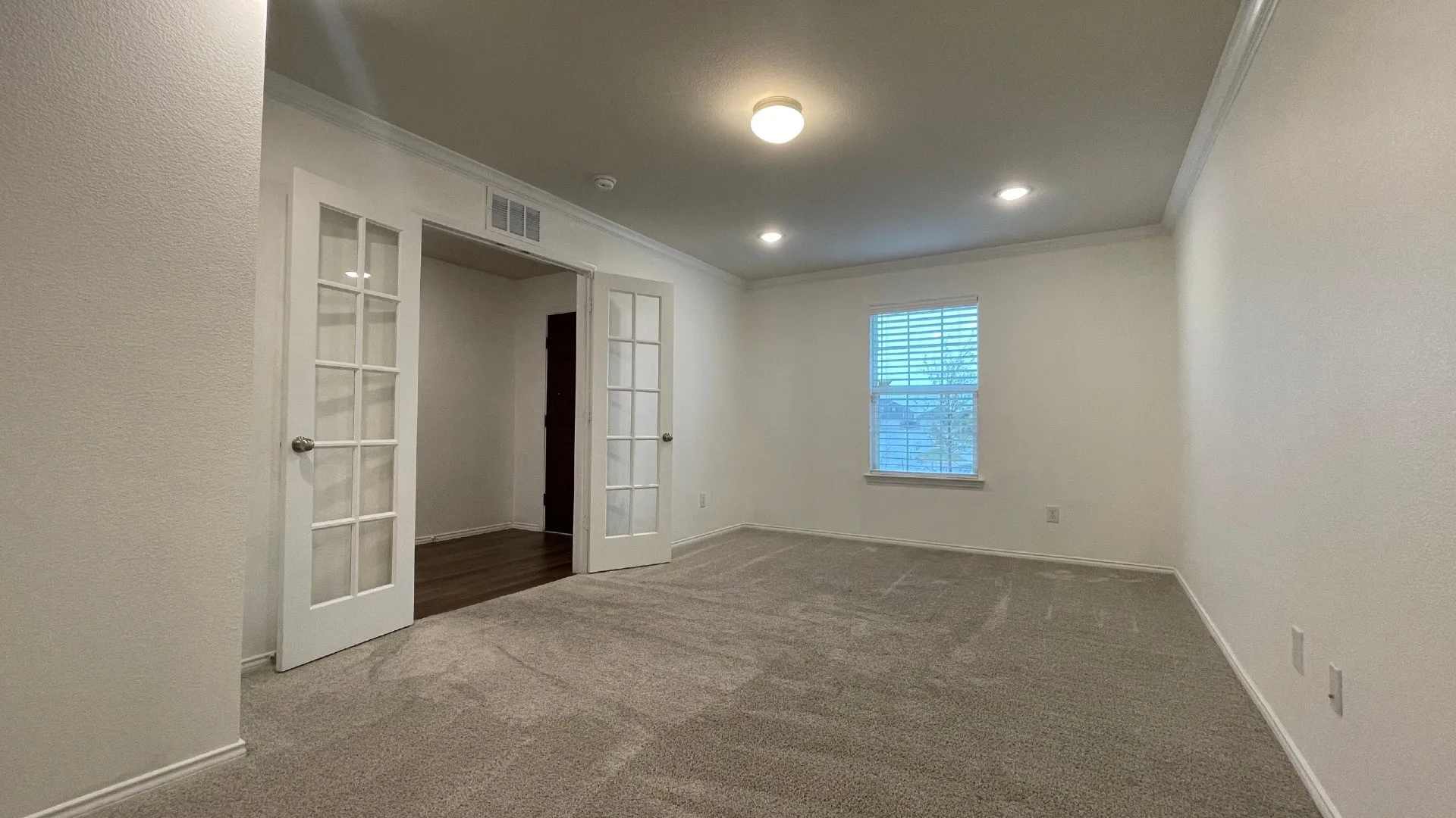 Bright and spacious room featuring recessed ceiling lighting, neutral wall finishes, carpet flooring, and multiple French doors with glass paneling providing natural light from the window