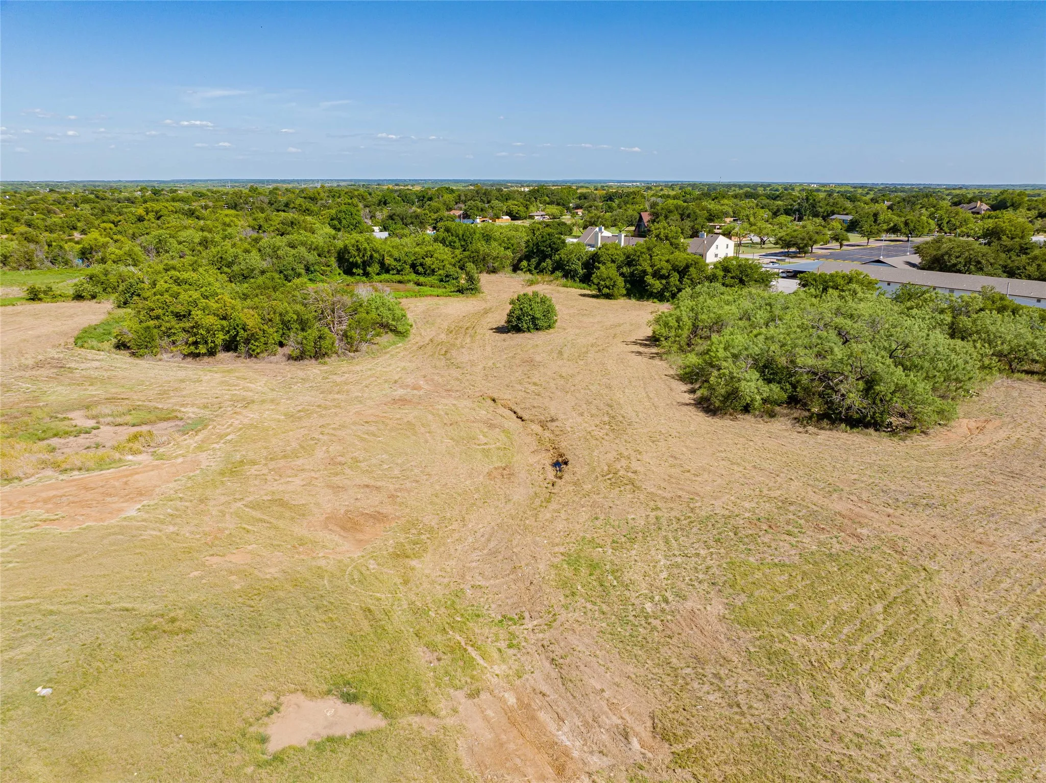 Expansive open land with interspersed mature trees, bordered by additional tree lines