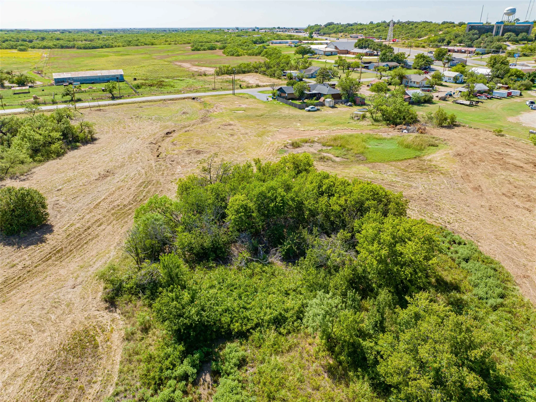 Expansive rural acreage featuring mature tree clusters, open pastureland, and established residential community in the distance
