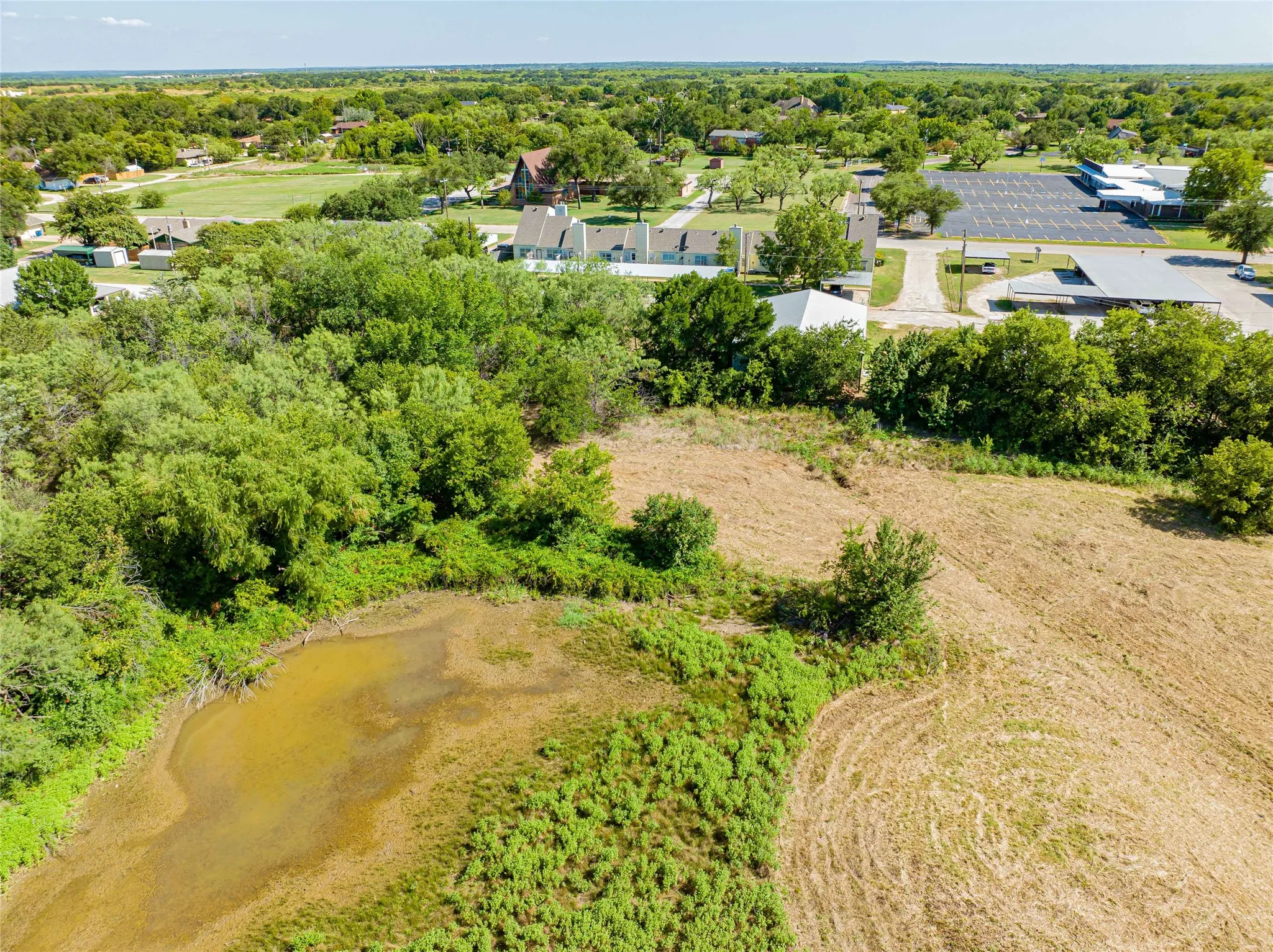 Aerial view showcasing expansive rural acreage with mature tree coverage, natural water feature, and established residential structures