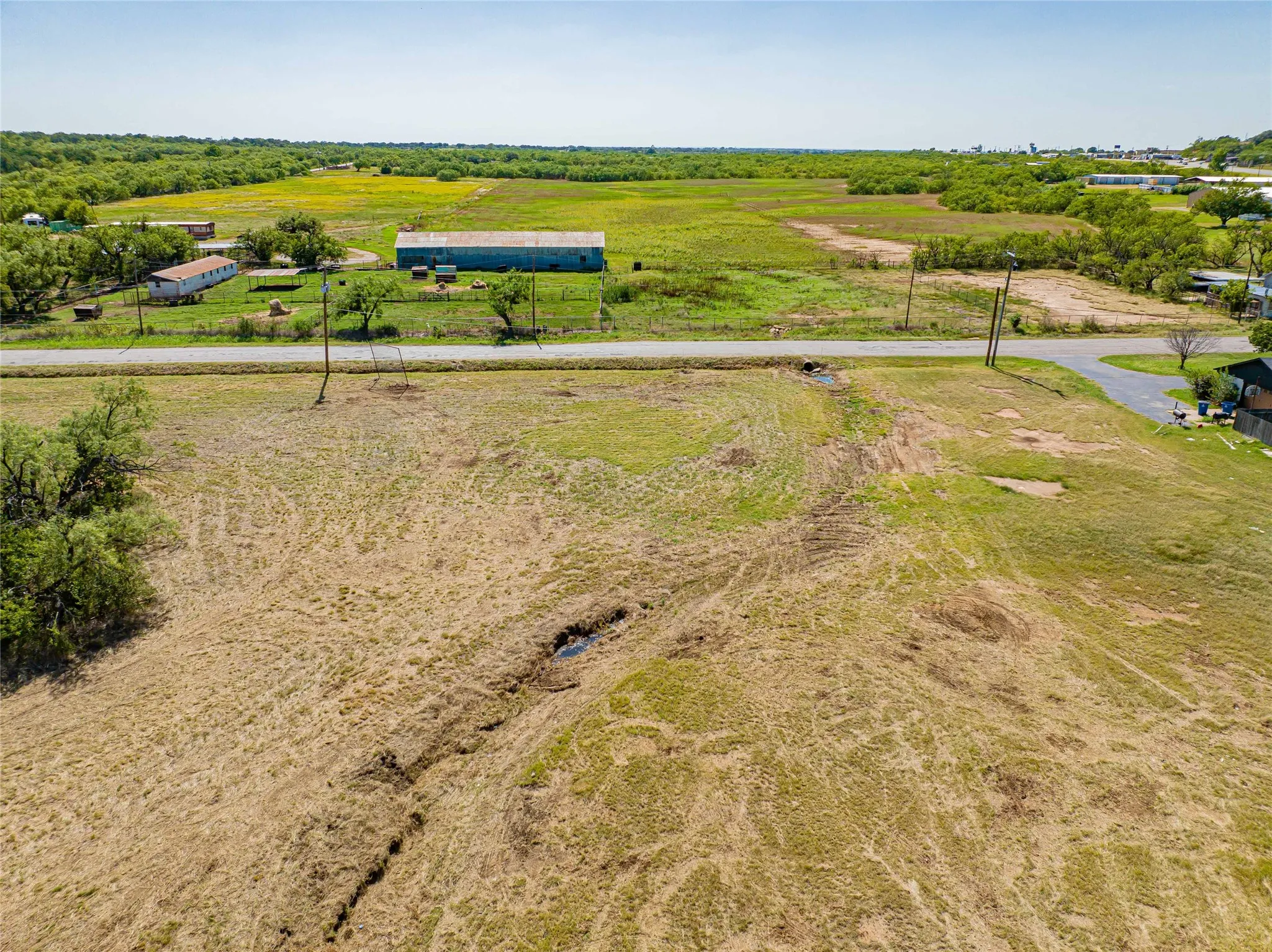 Sprawling rural acreage featuring expansive pastureland with mature tree coverage, a functional agricultural outbuilding with metal roof, and established fencing