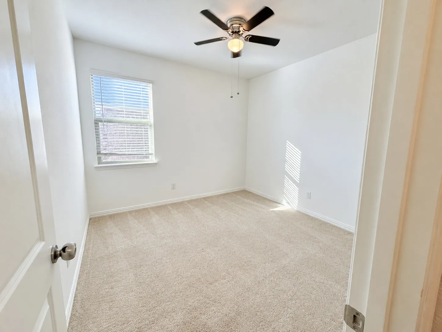 Neutral tone carpeting, single window with blinds, ceiling fan with integrated lighting, white walls