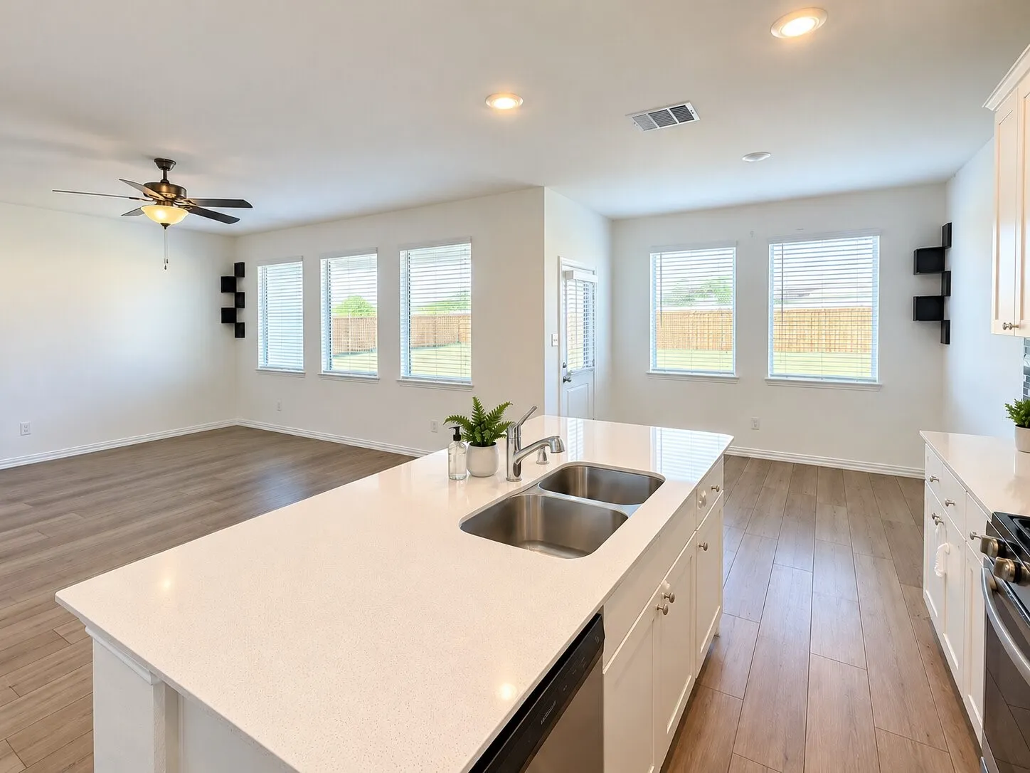 Kitchen island with double basin stainless steel sink and light-toned countertop, wood-finish flooring, recessed lighting, ceiling fan, and multiple windows