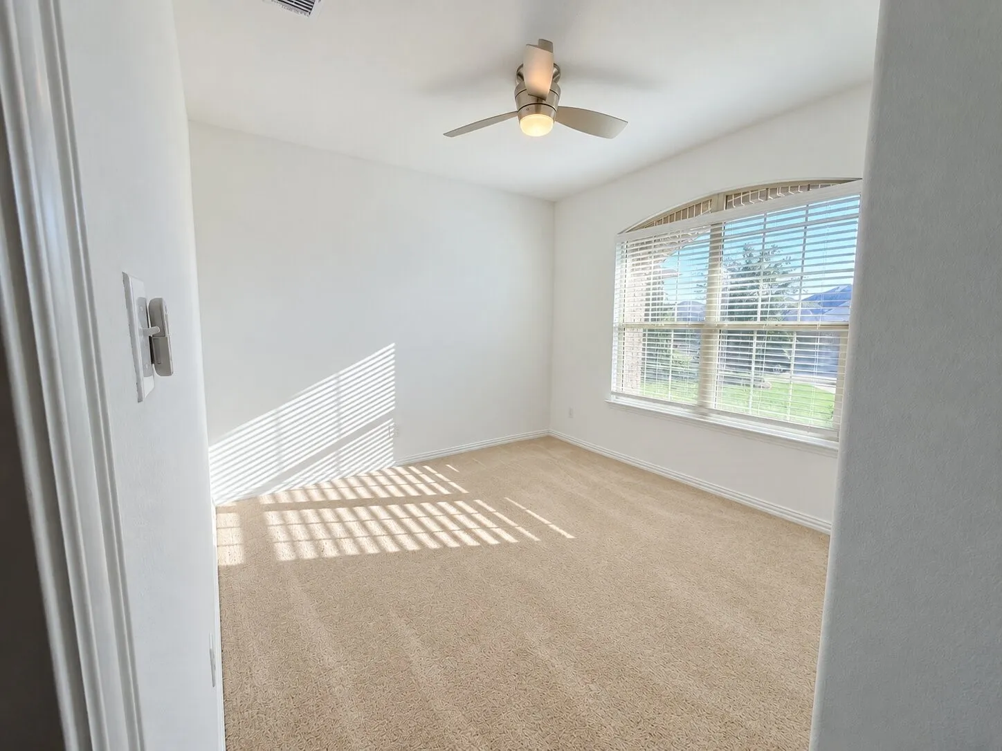 Arched window with horizontal blinds, neutral carpeting, and a ceiling fan with integrated lighting