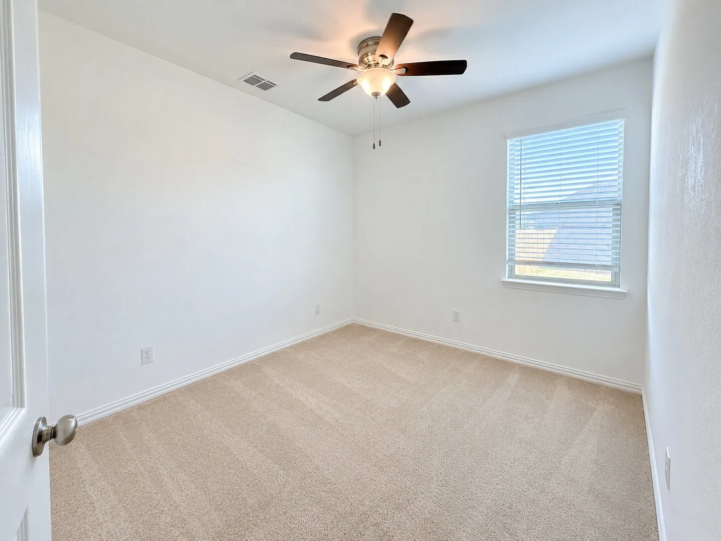 Light-colored carpeting, a window with horizontal blinds, and a ceiling fan with integrated lighting