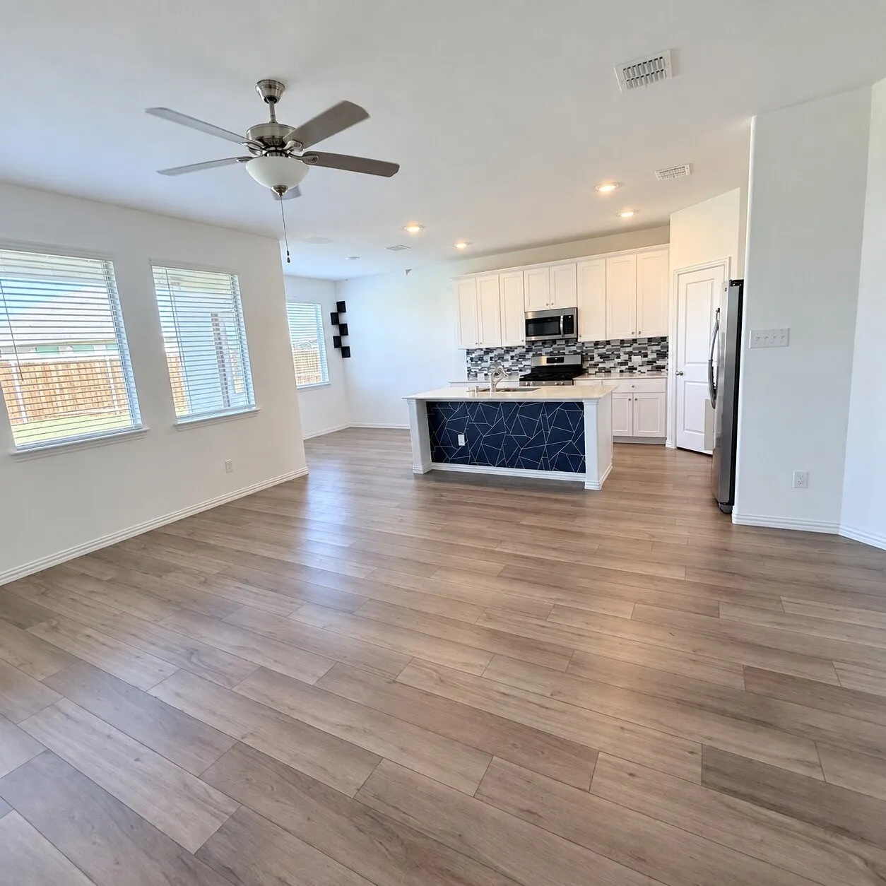 Open-concept living space featuring wood-finish flooring, a ceiling fan, and multiple windows