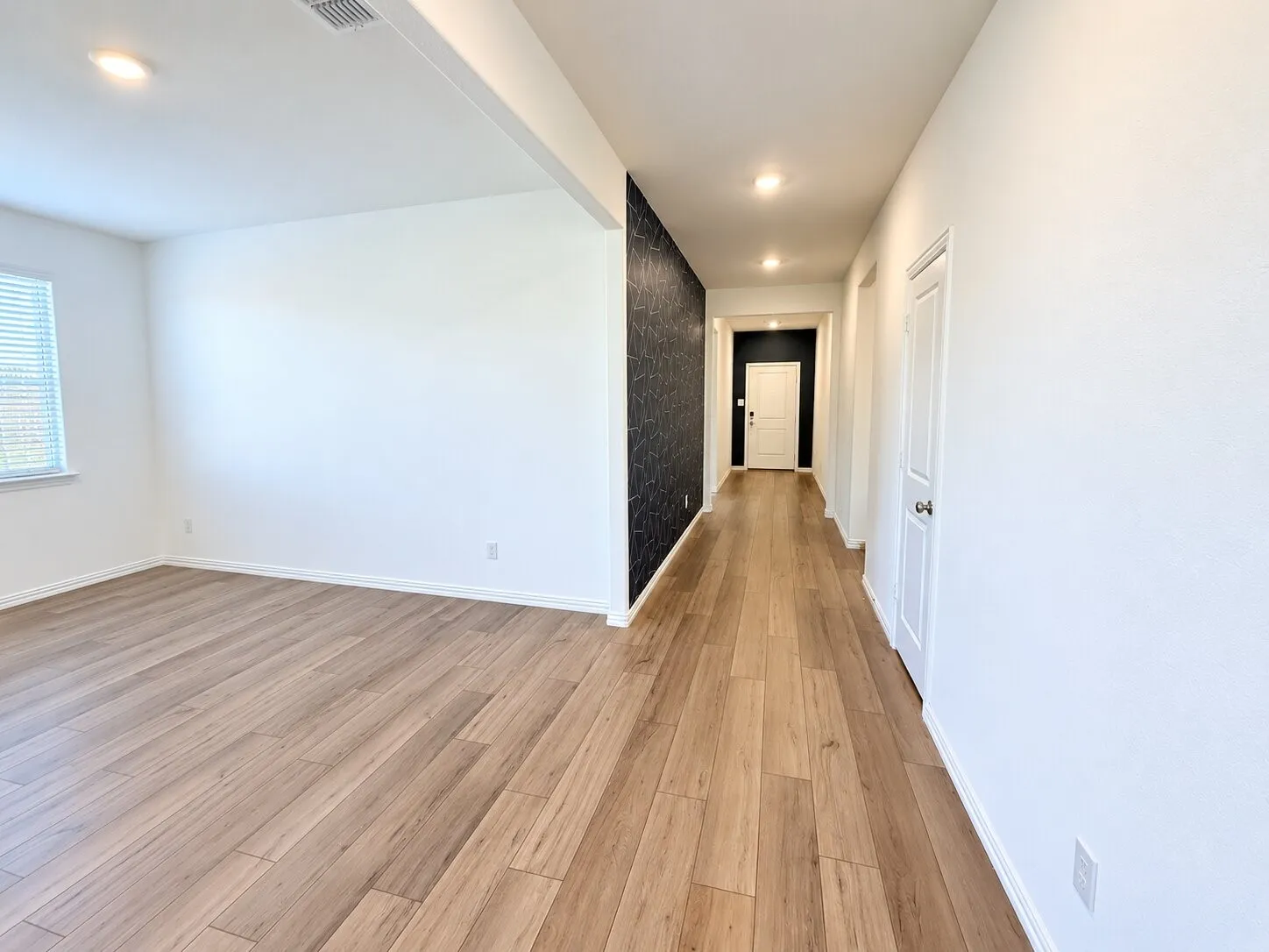 Spacious interior featuring wood-finish flooring, recessed lighting, a window with horizontal blinds, and a textured accent wall