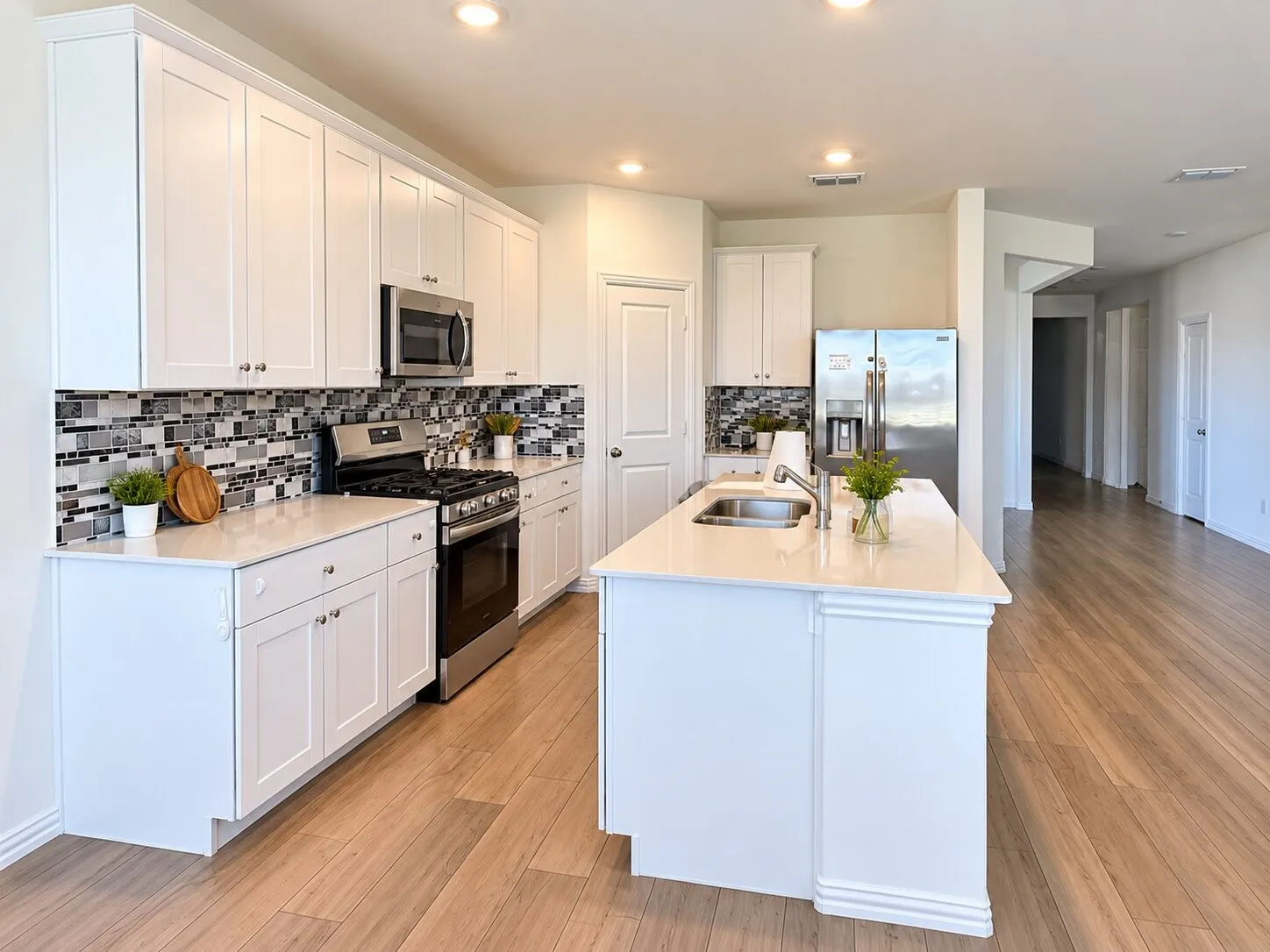 White shaker cabinetry, stainless steel appliances, mosaic tile backsplash, central island with sink, and wood-finish flooring