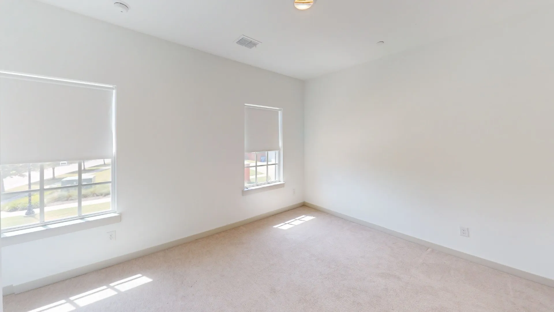 Neutral tone wall paint, two windows with roller shades, recessed ceiling lighting, and carpeted flooring