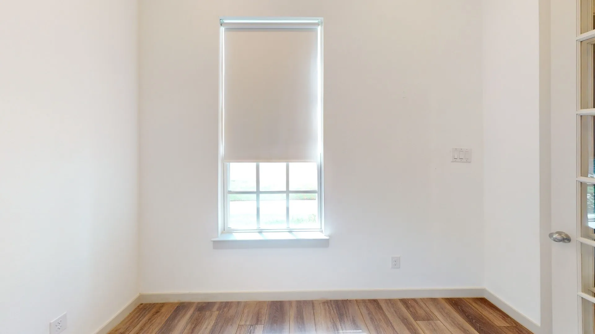 Bright corner room with large double-hung window featuring multiple panes, natural light, and roller shade