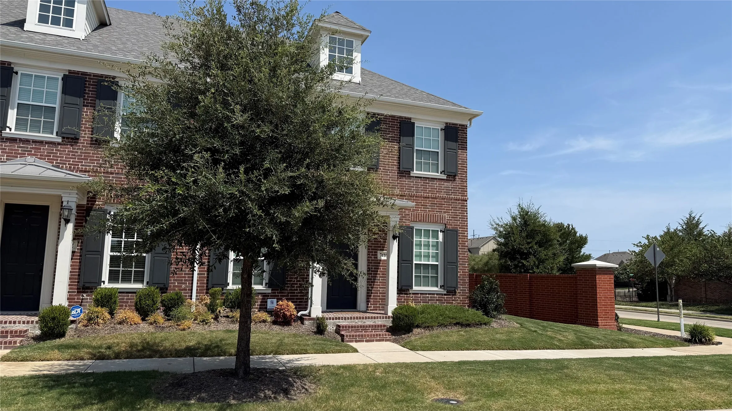 Brick exterior with dark shutters, front door with transom window, manicured landscaping, and mature trees