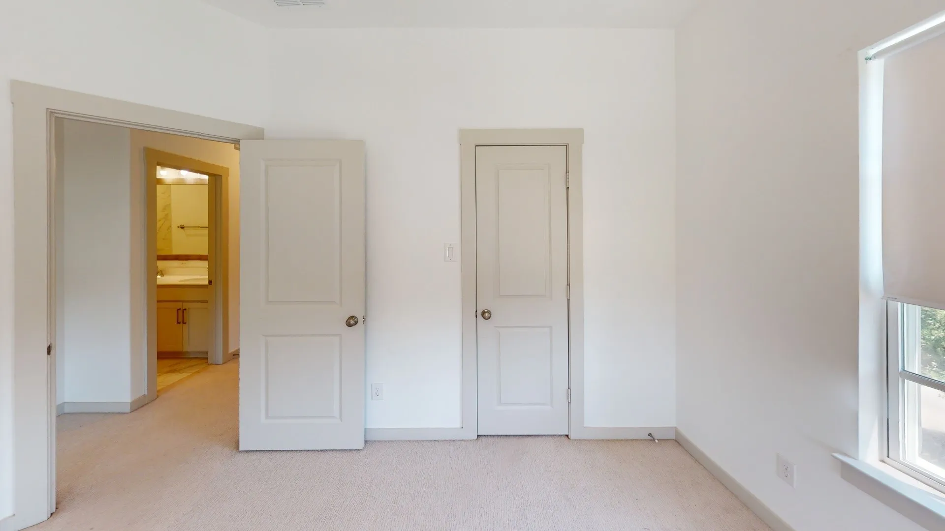 Bright, light-filled bedroom with multiple white six-panel doors, neutral carpet flooring, and abundant natural light from a large window