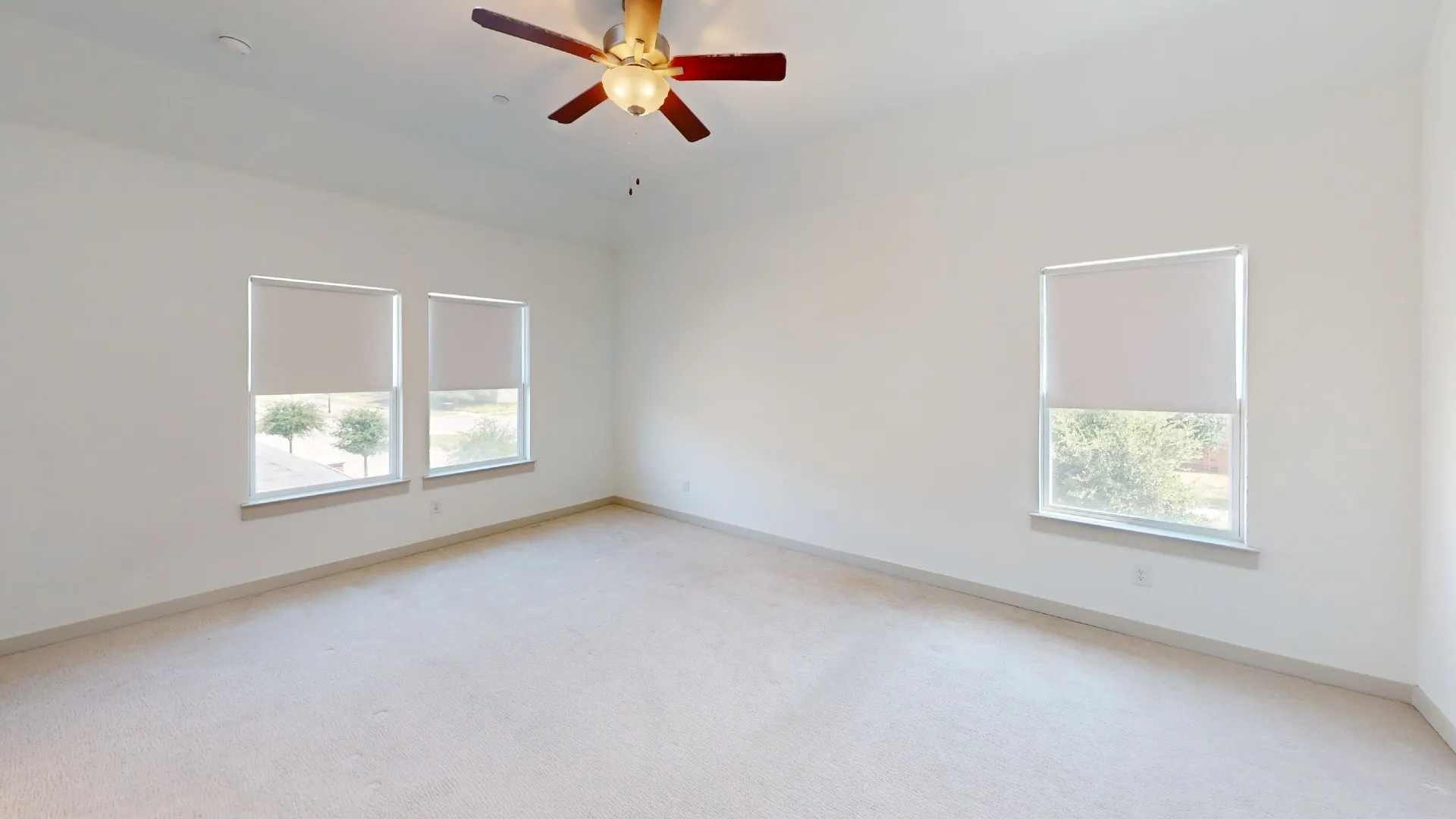 Expansive room featuring carpet flooring, multiple windows with roller shades, and a ceiling fan with integrated lighting
