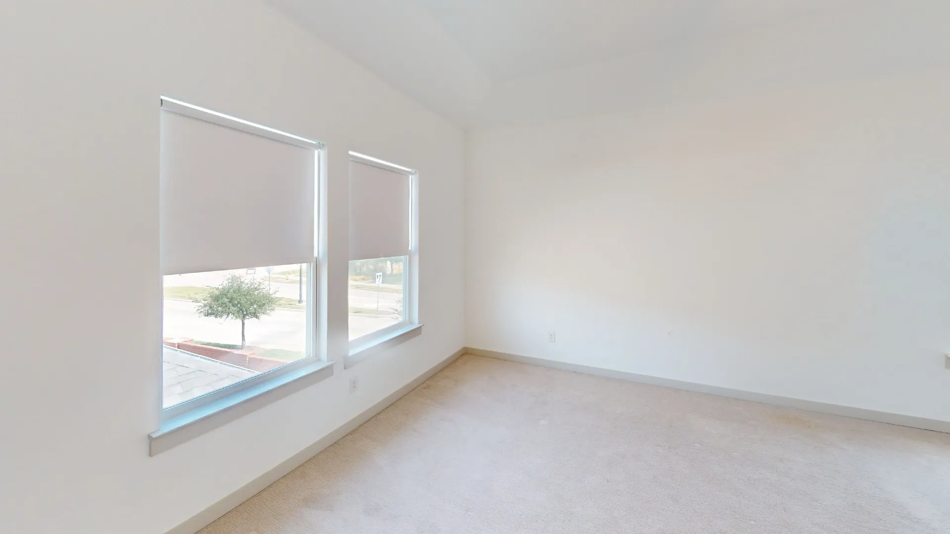 Bright, light-filled room with expansive windows featuring integrated roller shades, light wood-finish flooring, and clean white walls with crisp trim detailing