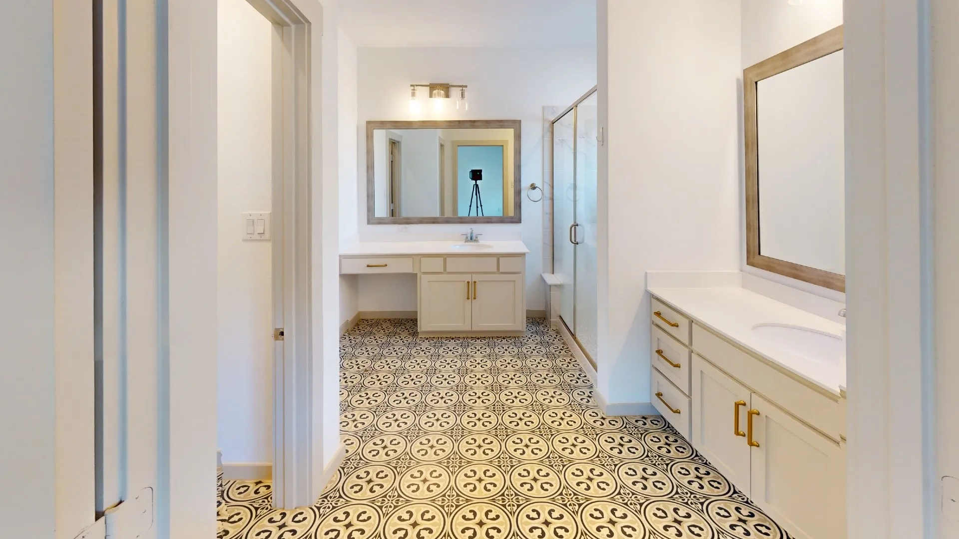 Dual vanity with white countertops, patterned tile flooring, walk-in shower with glass enclosure, and modern brass-finish​​‌​​​​‌​​‌‌​‌‌​​​‌‌​‌​‌​‌​​​‌​​ hardware