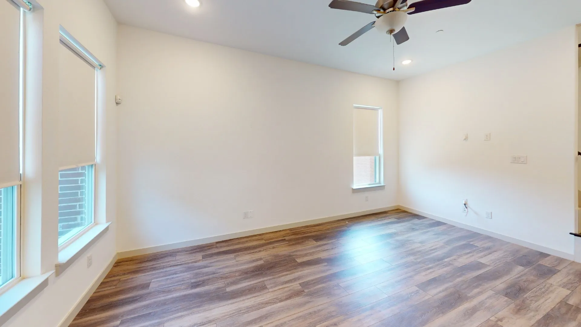 Bright, open room showcasing rich wood-finish flooring with warm tones and natural light from dual windows